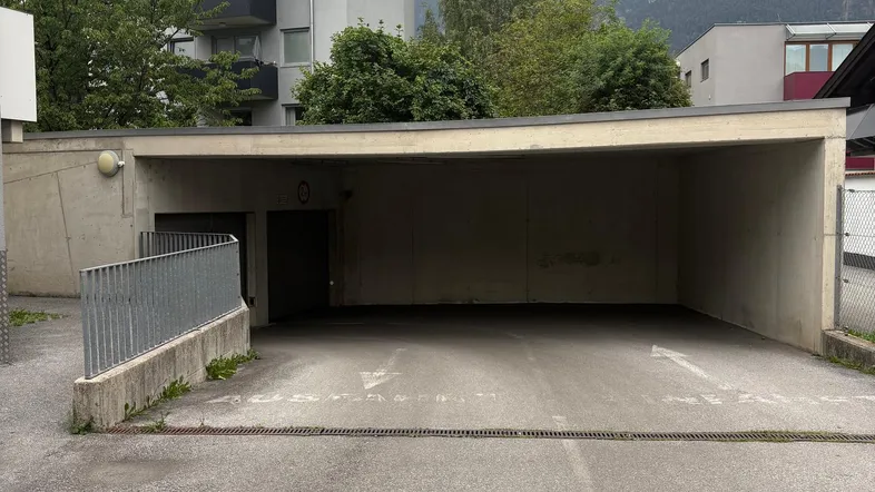 Überdachter Parkplatzbereich mit Betonkonstruktion und Blick auf die umliegenden Gebäude und Berge.