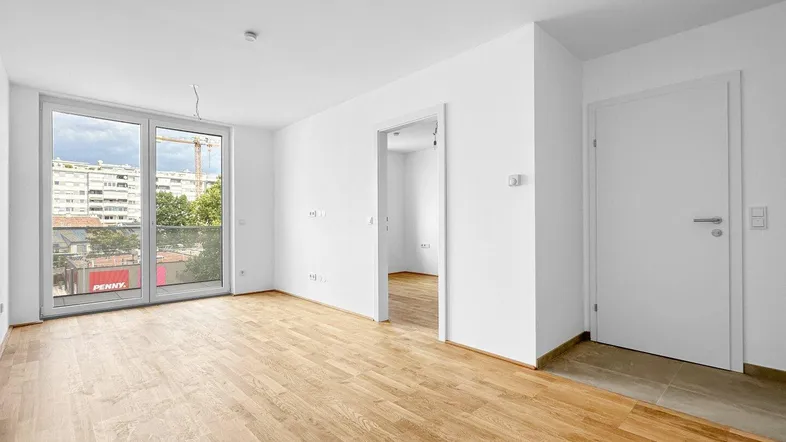 Helles, leeres Wohnzimmer mit Holzboden und Zugang zu einem französischen Balkon.