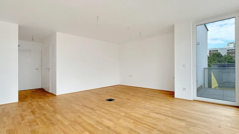 Heller, leerer Wohnbereich mit Parkettboden und Zugang zu einem kleinen Balkon.