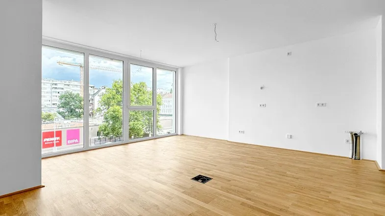 Heller, leerer Raum mit großen Fenstern und Holzboden, ideal für einen Wohnbereich.