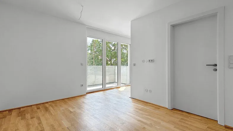 Heller Raum mit Parkettboden und Zugang zu einem Balkon, ideal für Wohn- oder Schlafbereich.
