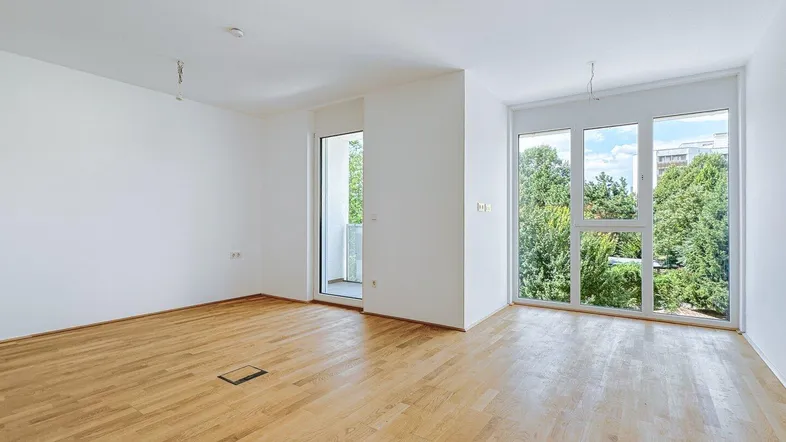 Helles Zimmer mit Holzboden, großen Fenstern und Zugang zu einem Balkon oder einer Terrasse.