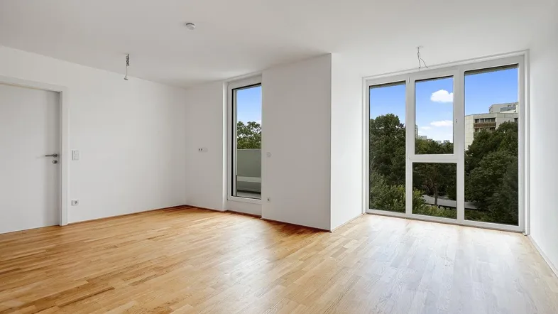 Helles Zimmer mit Holzboden, großen Fenstern und Zugang zu einem Balkon, bietet einen grünen Ausblick.