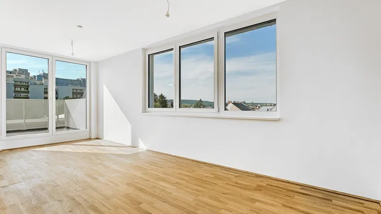 Helles Zimmer mit großen Fenstern, Holzboden und Zugang zu einem Balkon mit Stadtblick.