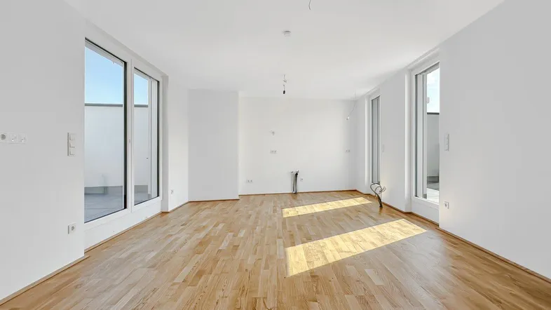 Helles, leeres Zimmer mit Holzboden und großen Fenstern, die Zugang zu einem Außenbereich bieten.