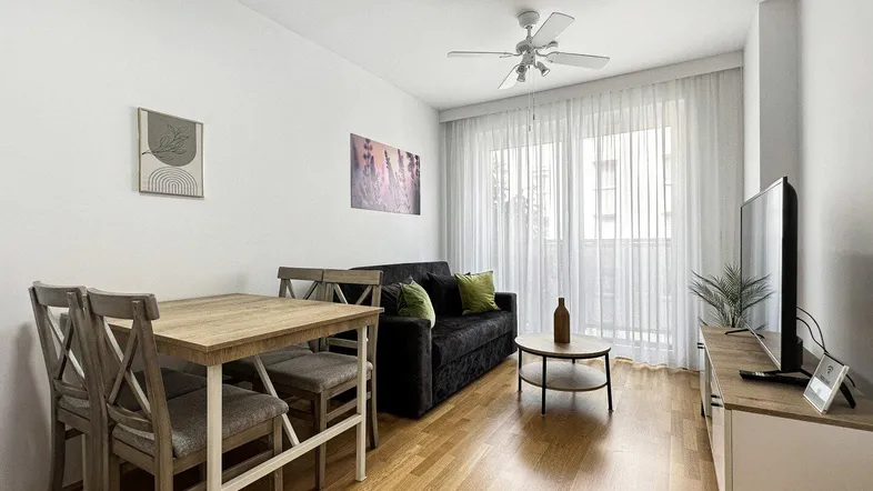 Helles Wohn- und Esszimmer mit Holzboden, bequemer Couch und Esstisch. Große Fenster lassen viel Tageslicht herein.