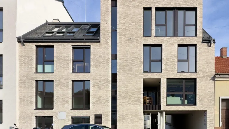 Modernes Mehrfamilienhaus mit heller Ziegelfassade, großen Fenstern und Tiefgaragenzufahrt.