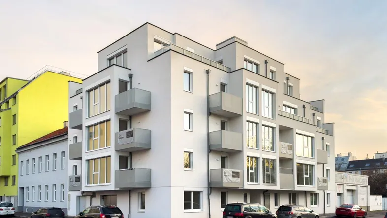 Modernes Mehrfamilienhaus mit klarer Architektur, großen Fenstern und mehreren Balkonen in städtischer Umgebung.