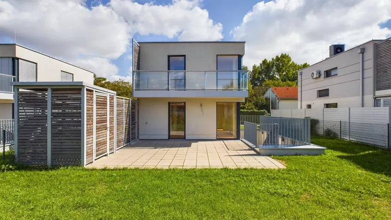 Moderne Reihenhausfassade mit großer Terrasse, Garten und Balkon unter blauem Himmel.