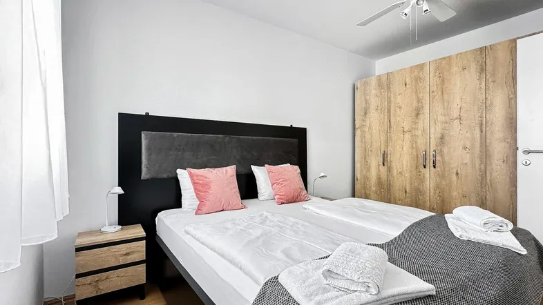 Helles Schlafzimmer mit Doppelbett, Holzschrank und Deckenventilator für angenehme Nächte.