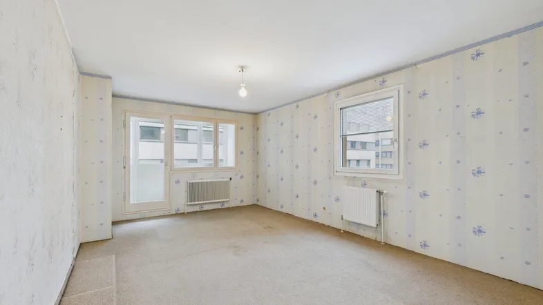 Geräumiges Zimmer mit Teppichboden, Fenster und Zugang zu einem Außenbereich, renovierungsbedürftig.