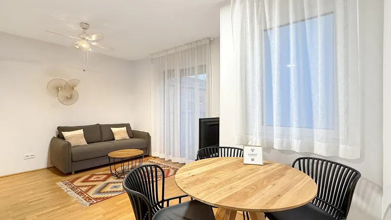 Helles Wohn- und Esszimmer mit Parkettboden, Deckenventilator und Zugang zu einem Balkon.