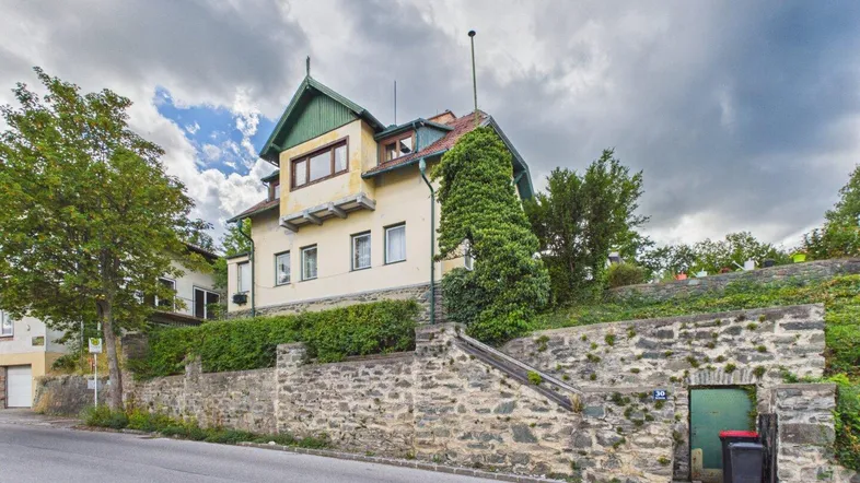 Historisches Gebäude mit gelber Fassade, grünem Dach und Steinfundament an einer Straße.