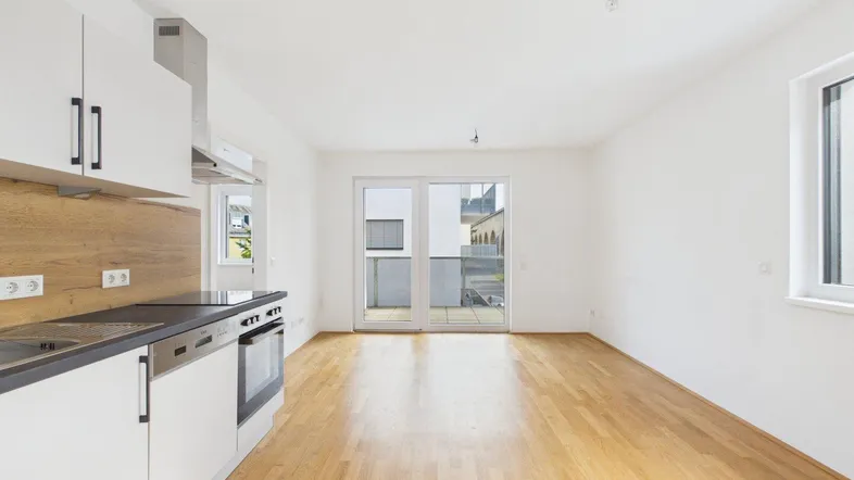 Heller offener Wohn-Essbereich mit moderner Einbauküche, Parkettboden und Zugang zum Balkon.