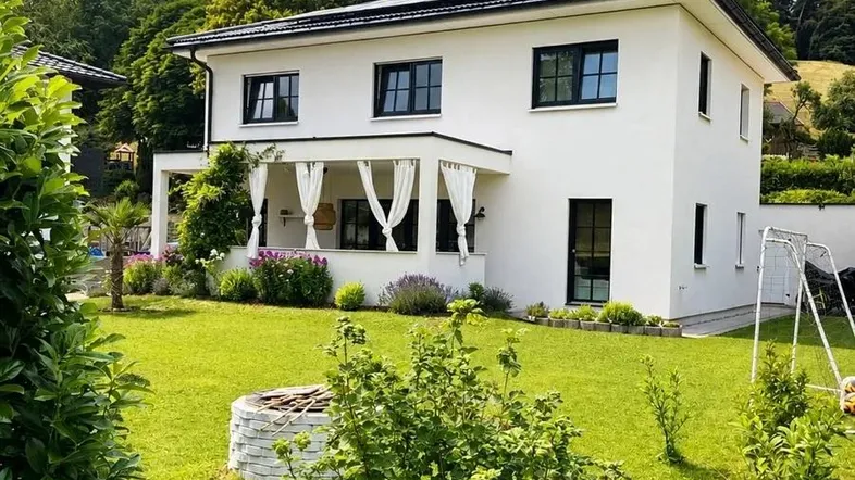 Weißes Einfamilienhaus mit großem grünen Garten und sonniger Terrasse.