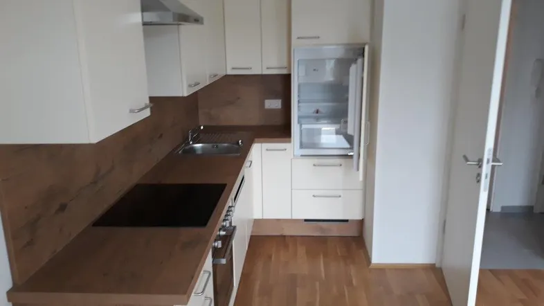 Moderne Einbauküche mit hellen Schränken, Holzoptik-Arbeitsplatten und integrierten Geräten.