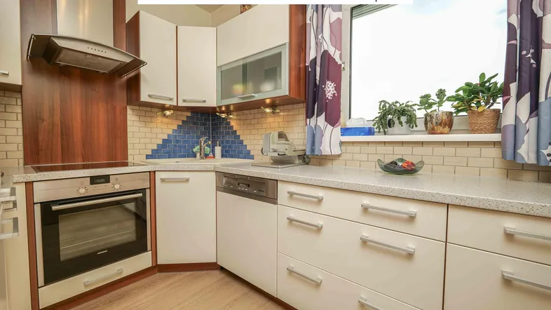 Funktionale Küche mit hellen Fronten, blauen Fliesen und Fensterblick ins Grüne.