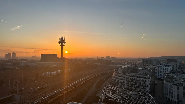 Panoramablick über die Stadt bei Sonnenuntergang mit Bahngleisen und Gebäuden im Vordergrund.