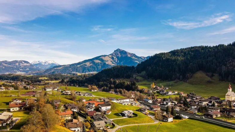 Panoramablick auf ein malerisches Dorf in den Alpen, umgeben von grünen Hügeln und majestätischen Bergen.