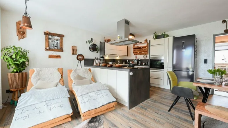 Gemütlicher offener Wohnbereich mit integrierter Küche, Holzboden und bequemen Lounge-Sesseln.