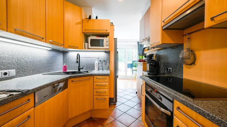 Helle Küche mit Holzschränken, dunkler Arbeitsplatte und Terrakottafliesen, mit Zugang zum Außenbereich.