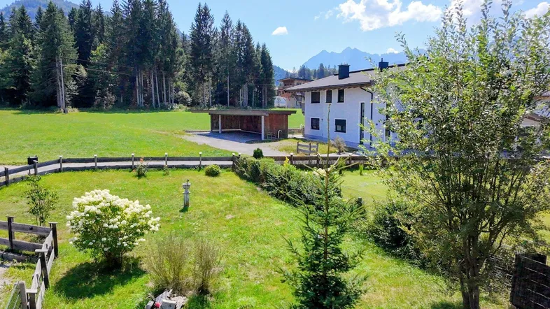 Großzügiger Gartenbereich mit Rasenfläche, Bäumen und Blick auf die Berge.