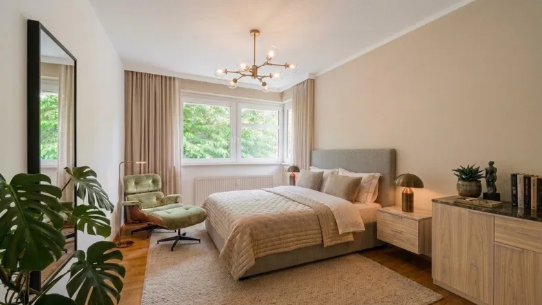 Ruhiges Schlafzimmer mit Doppelbett, Sessel und großen Fenstern mit Blick ins Grüne.