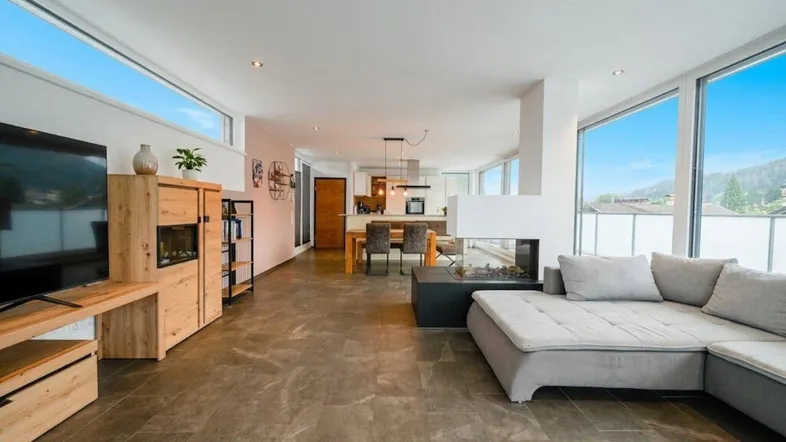 Helles, offenes Wohn- und Esszimmer mit modernem Kamin, großen Fenstern und Blick auf die Berge.
