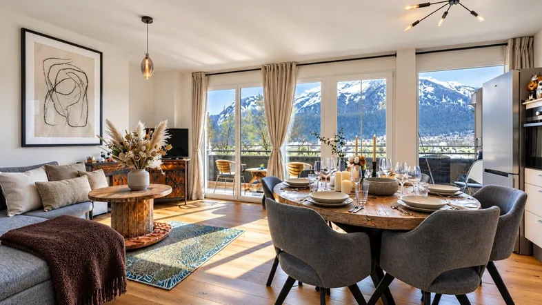 Heller offener Wohn- und Essbereich mit Holzboden, modernen Möbeln und Bergblick.