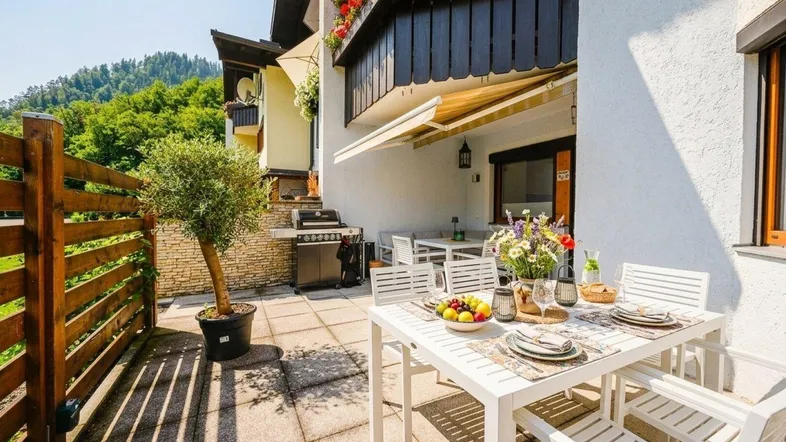 Große gepflasterte Terrasse mit Esstisch, Grillbereich und Blick auf die umliegende Natur.