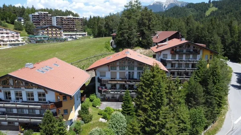 Luftaufnahme von traditionellen Gebäuden mit roten Dächern in einer bergigen, bewaldeten Landschaft.