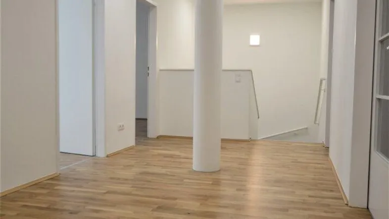 Heller Flur mit Holzboden und einer zentralen Säule, der zu verschiedenen Räumen führt.