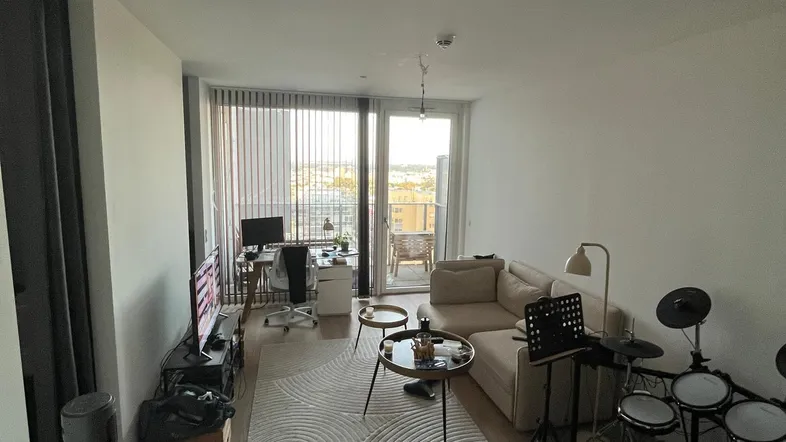 Helles Wohnzimmer mit Holzboden, beigem Sofa und Zugang zu einem Balkon mit Stadtblick.