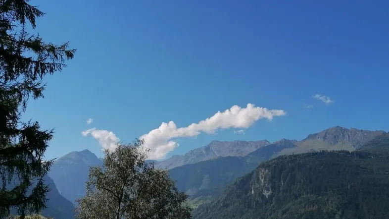 Malerischer Bergblick unter blauem Himmel mit einigen Wolken und Bäumen im Vordergrund.