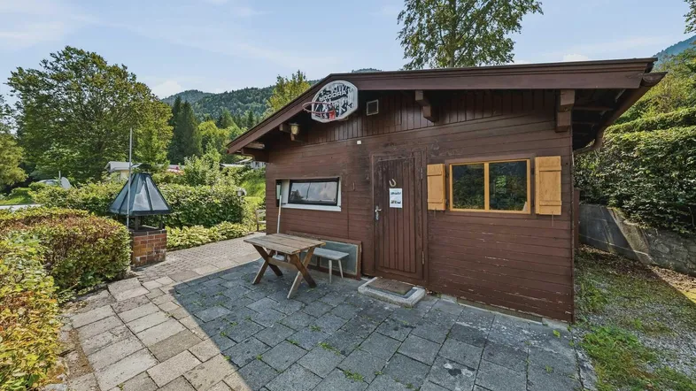 Gemütliche Terrasse vor einer Holzhütte mit Grillplatz und Blick auf die umliegende Natur.