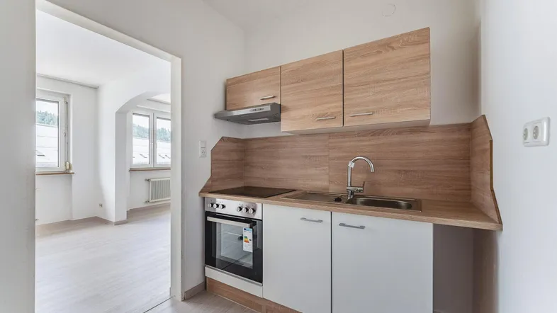 Kleine, funktionale Küchenzeile mit Holzoptik-Schränken und integriertem Backofen in hellem Raum.
