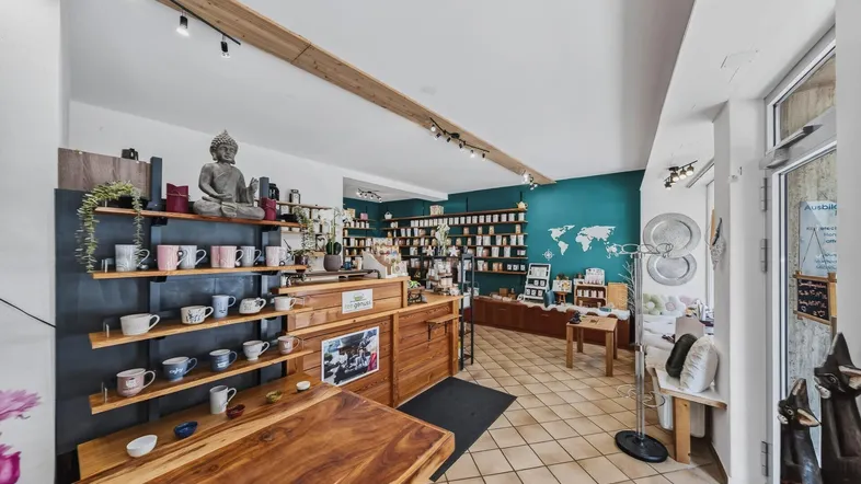 Innenansicht eines Teeladens mit Holzelementen, Regalen voller Produkte und einer Buddha-Statue.