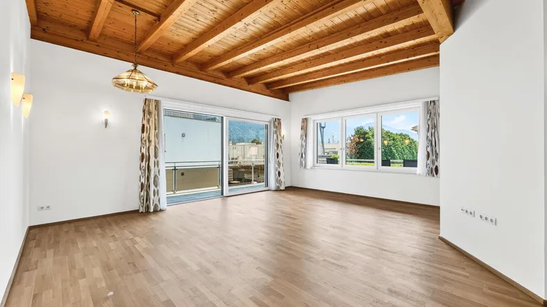 Helles Wohnzimmer mit Holzbalkendecke, Parkettboden und Zugang zum Balkon.