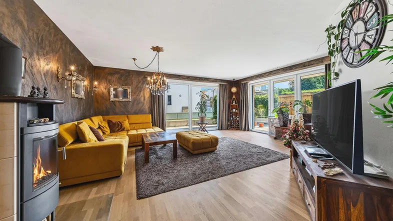 Helles Wohnzimmer mit Kaminofen, gelbem Ecksofa und Zugang zur Terrasse.