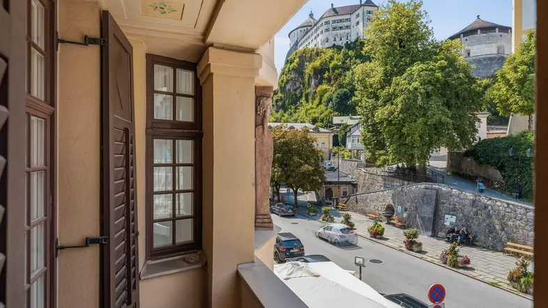Blick von einem Balkon auf eine historische Straße mit einem imposanten Schloss auf einem Hügel im Hintergrund.