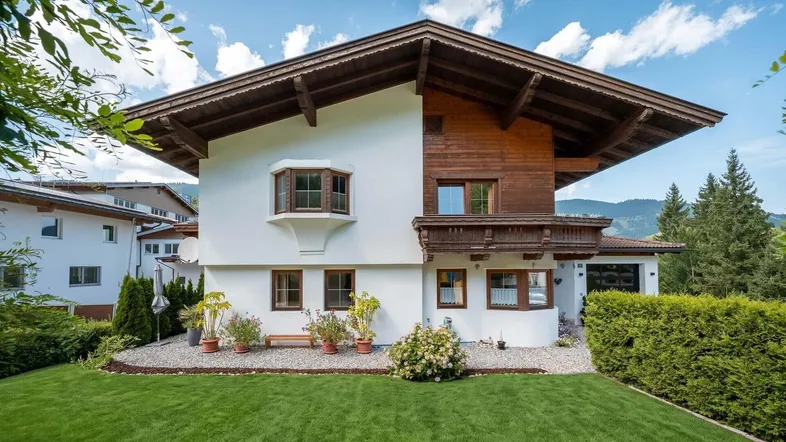 Traditionelles Haus im alpenländischen Stil mit weißer Fassade, Holzelementen und gepflegtem Vorgarten.