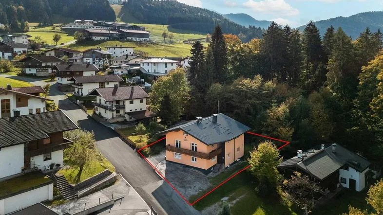Luftaufnahme des Hauses mit Grundstücksgrenzen, umgeben von grüner Landschaft und Bergen.