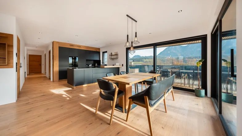 Heller, offener Wohn- und Essbereich mit moderner Küche, Holzboden und Zugang zur Terrasse mit Bergblick.
