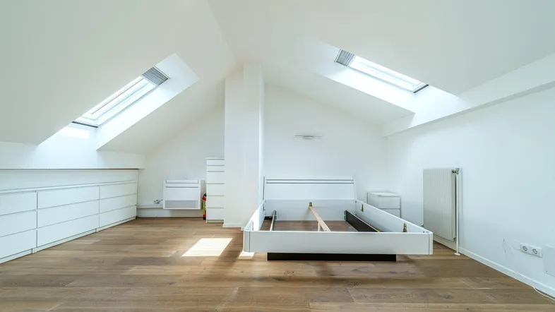 Helles Schlafzimmer im Dachgeschoss mit Holzboden, Dachfenstern und weißen Einbauschränken.