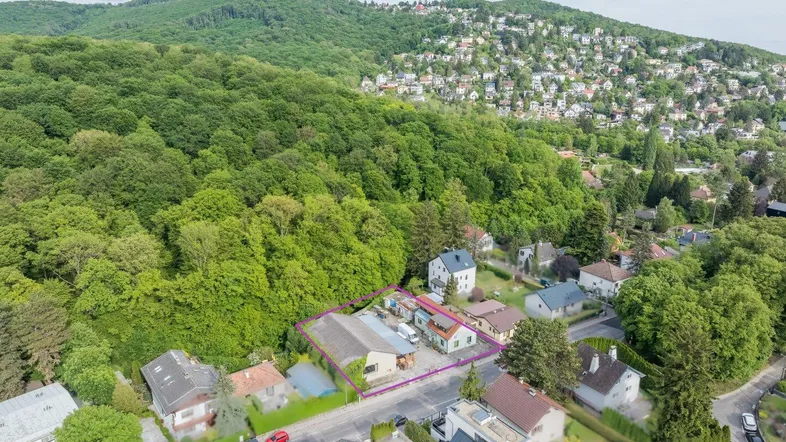 Luftaufnahme eines Wohngebiets mit viel Grün und einem markierten Grundstück am Waldrand.