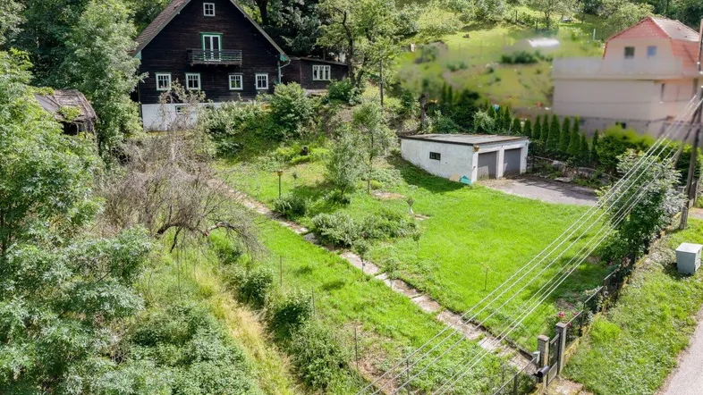 Dunkles Holzhaus mit weißem Sockel und Satteldach, umgeben von viel Grün und einem Gartenbereich.