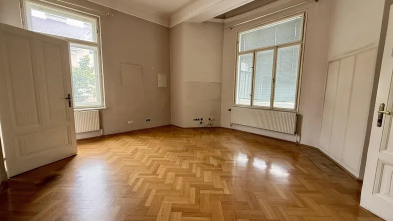 Geräumiges Zimmer mit Fischgrätparkett und hohen Fenstern, ideal als Wohn- oder Schlafzimmer.