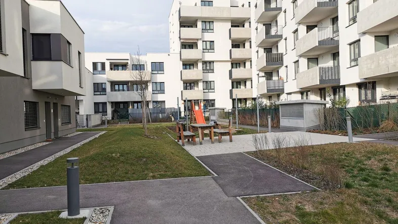 Moderne Wohngebäude mit weißer Fassade und einem gemeinschaftlichen Grünbereich mit kleinem Spielplatz.