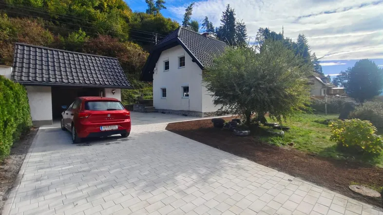 Einfamilienhaus mit gepflasterter Auffahrt, Garage und umgebender grüner Landschaft.