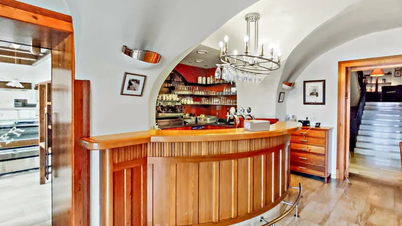 Gewölbter Barbereich mit Holztheke, Kronleuchter und Blick auf eine Treppe.